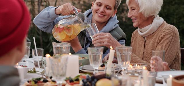 Young woman pouring a drink for an older woman. They are sitting together at a table.